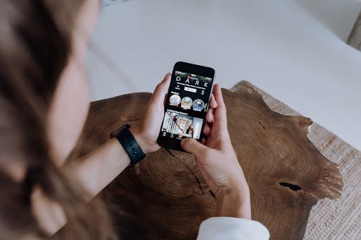 An adult browsing a streaming app on a smartphone while sitting at a wooden table.